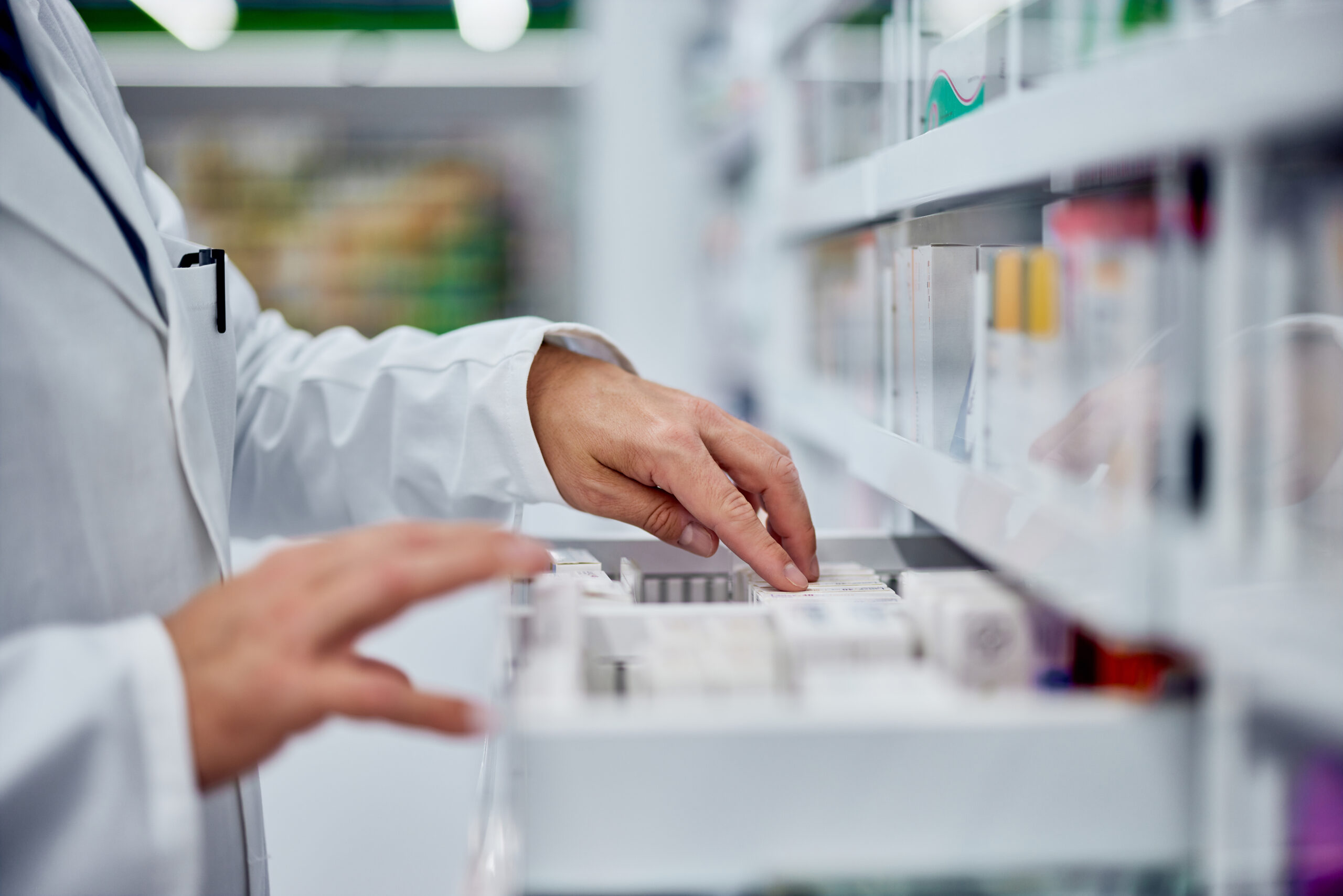 A person in white lab coat and gloves looking at medicine.