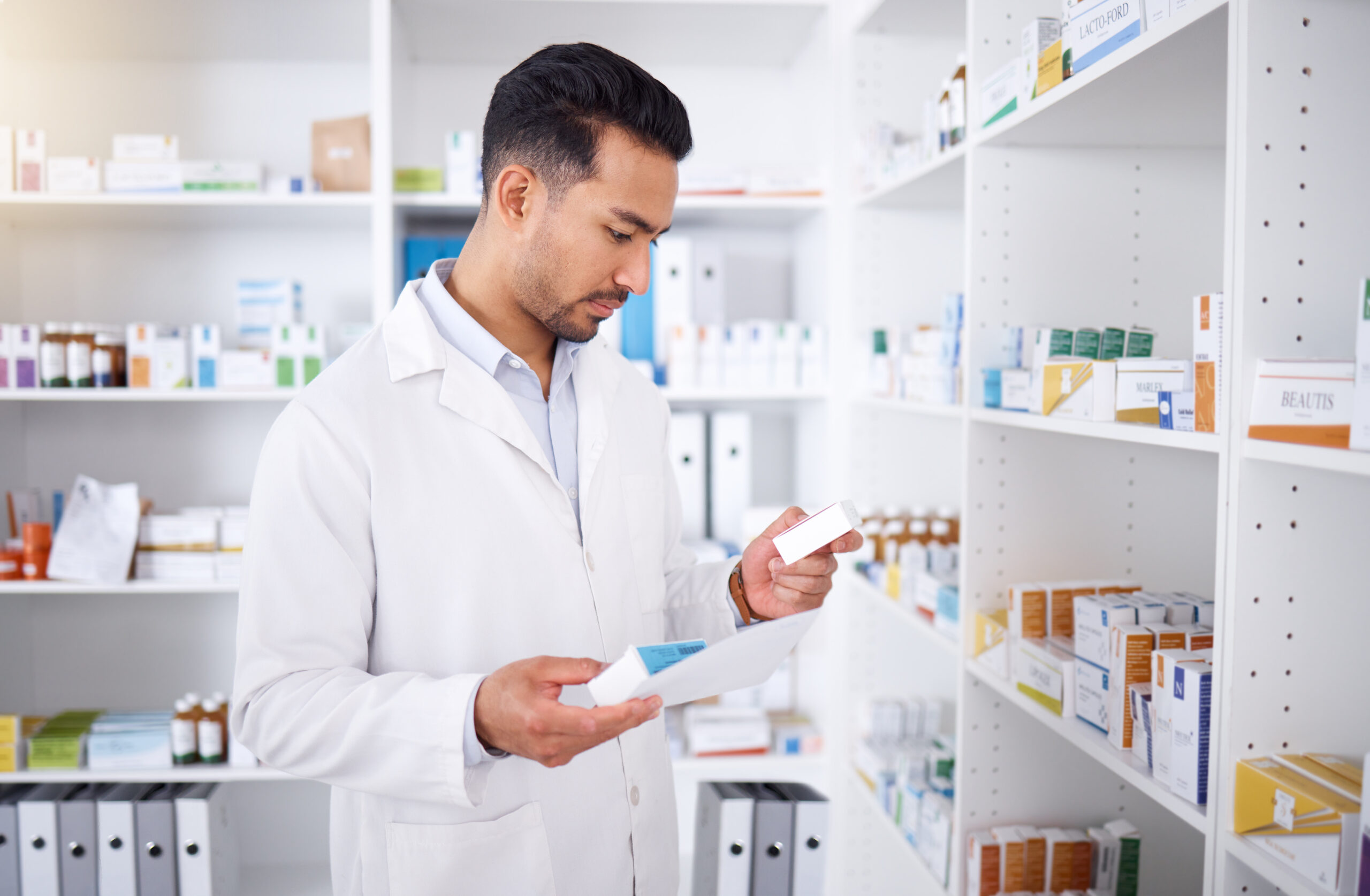 Medicine inspection, pharmacy and man with a note for medical stock or healthcare in store. Retail, work and male Asian pharmacist reading information on a box of pills with a document for inventory