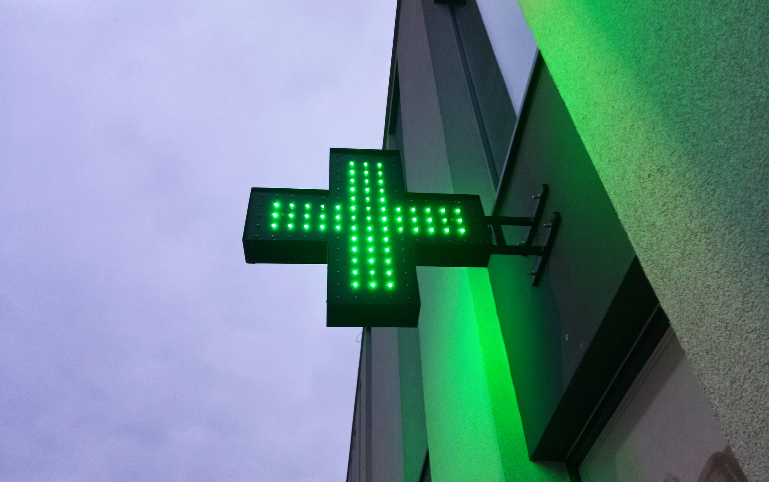 A green lit up cross sign on the side of a building.